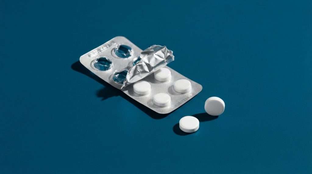 Blíster de comprimidos abierto sobre fondo azul intenso, con tres pastillas sueltas y una sombra marcada